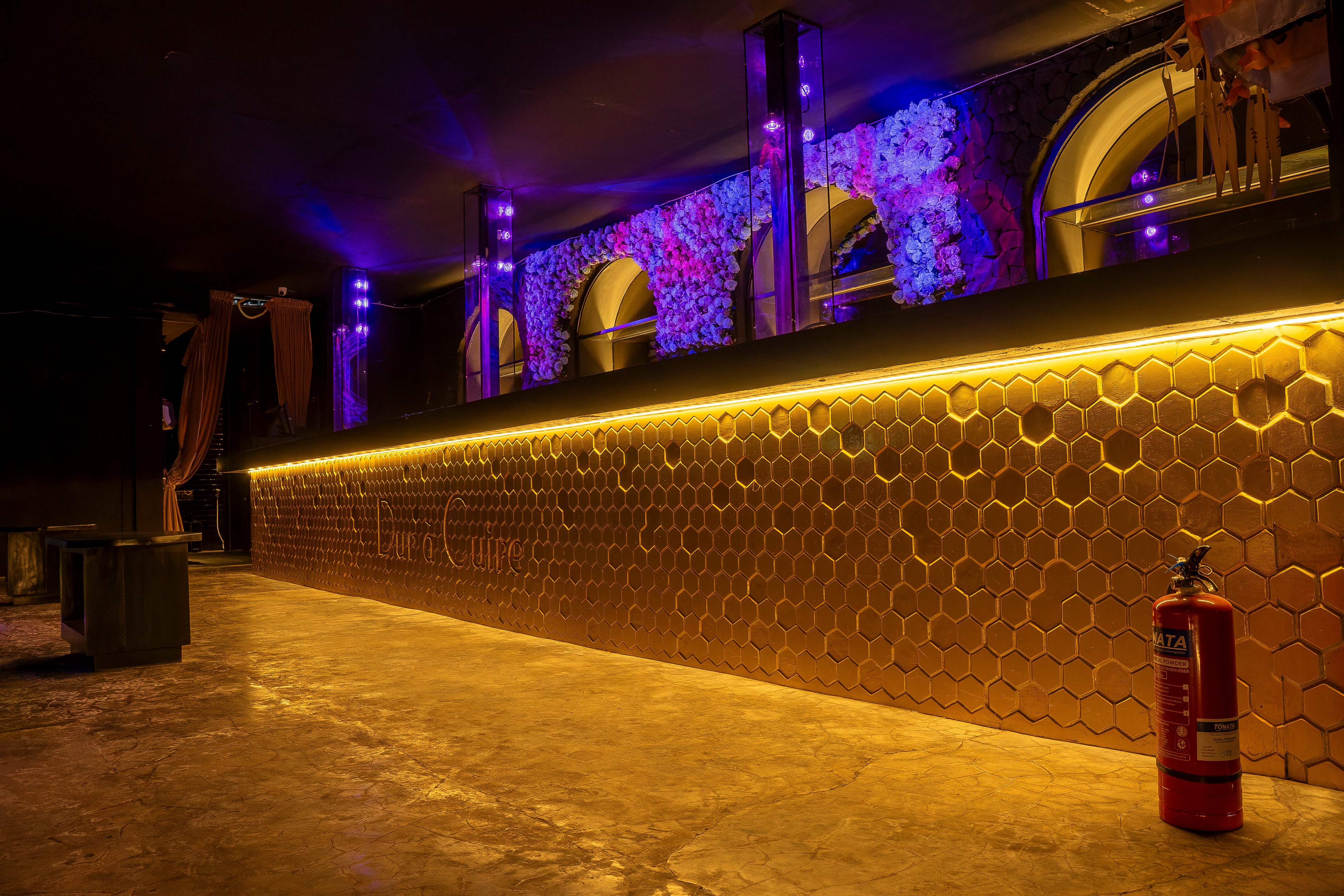 Long honeycomb bar with golden lighting and purple flower installation